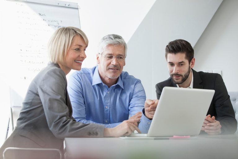 Three professionals discussing ideas while looking at a laptop in a modern office setting.