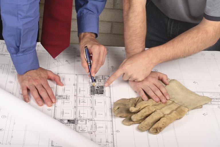 Hands pointing at architectural plans, with work gloves nearby on the table.
