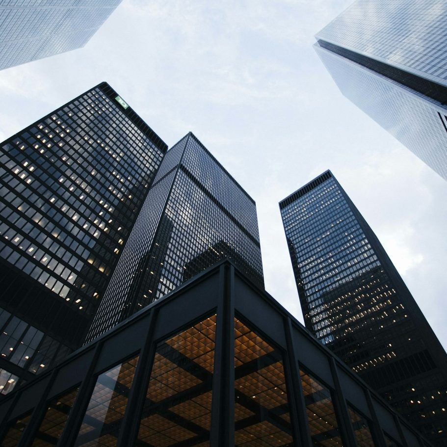 Skyward view of tall buildings with glass facades against a cloudy sky.