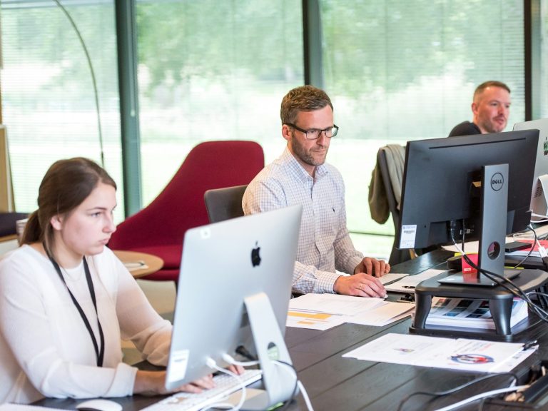 monthly it support plans Three people working at computers in a modern office setting.