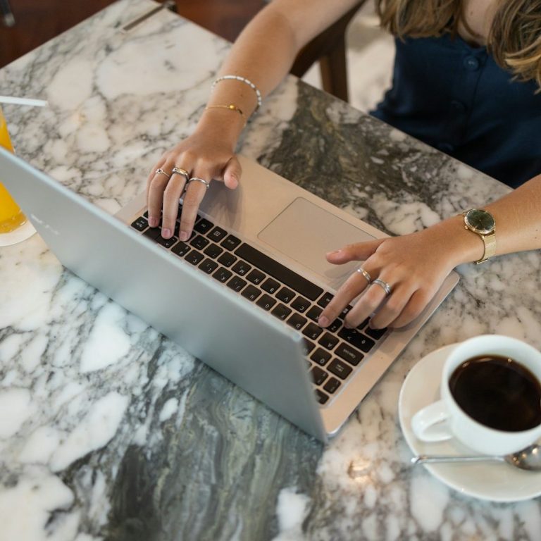 Our Story Person typing on a laptop at a table with a coffee cup and a drink.
