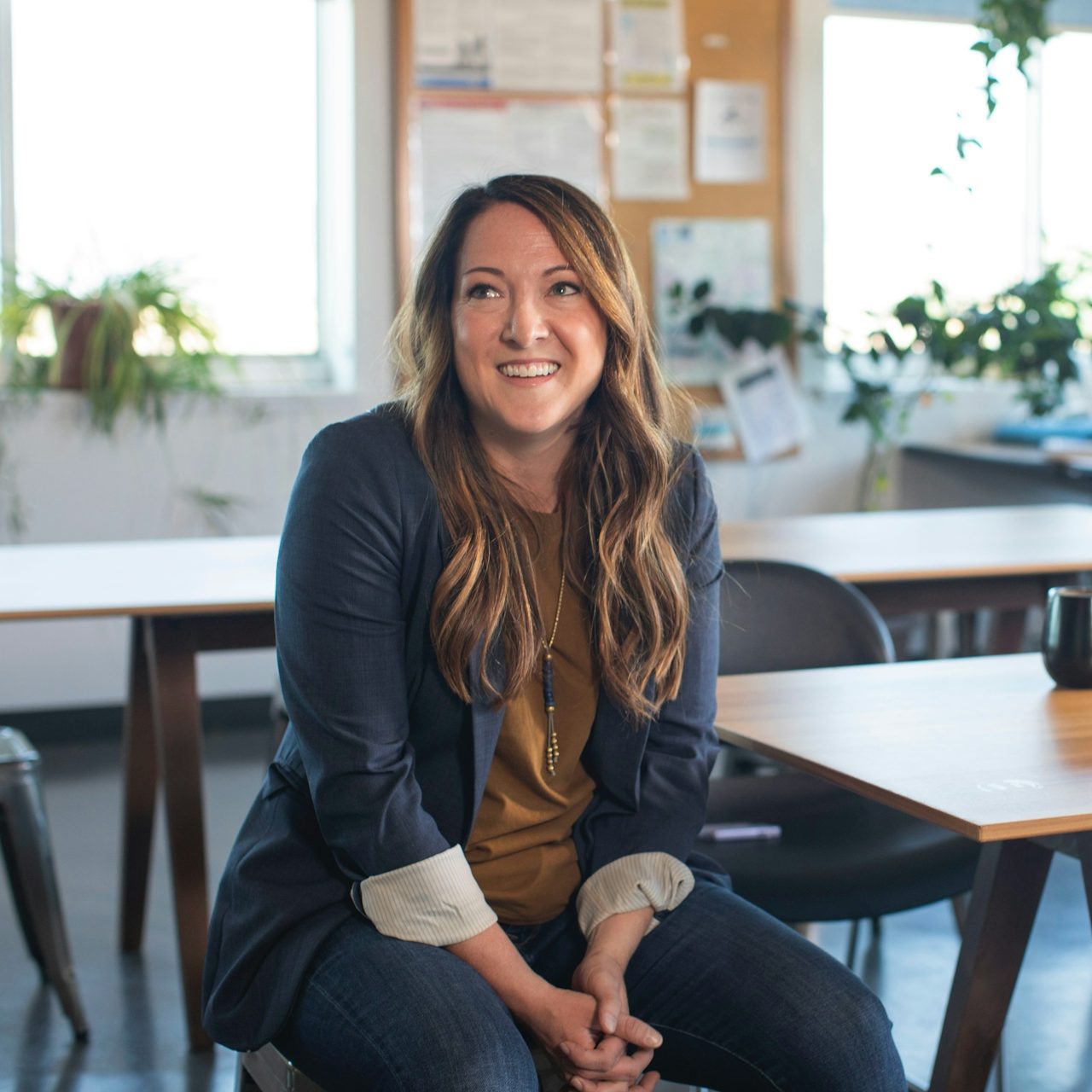 Why choose us Smiling woman sitting at a table in a bright, plant-filled office.