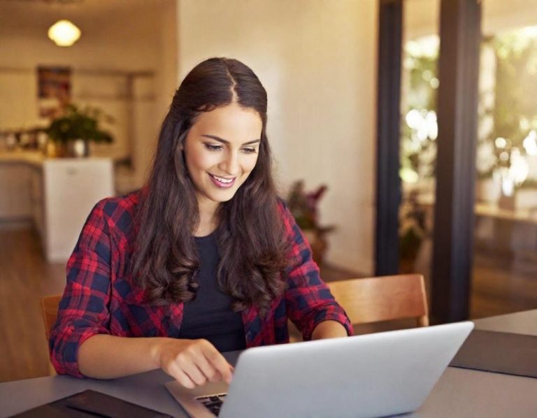 device migration Smiling woman using a laptop at a table in a bright indoor environment.
