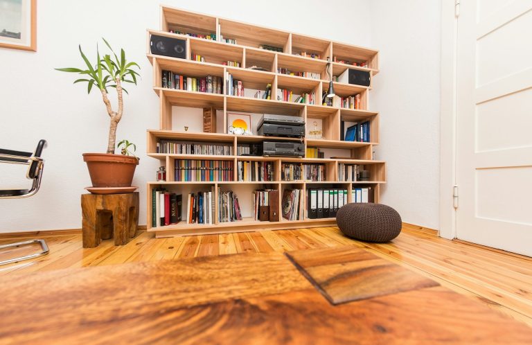 Wooden bookshelf filled with books, a plant, and a chair on a wooden floor.