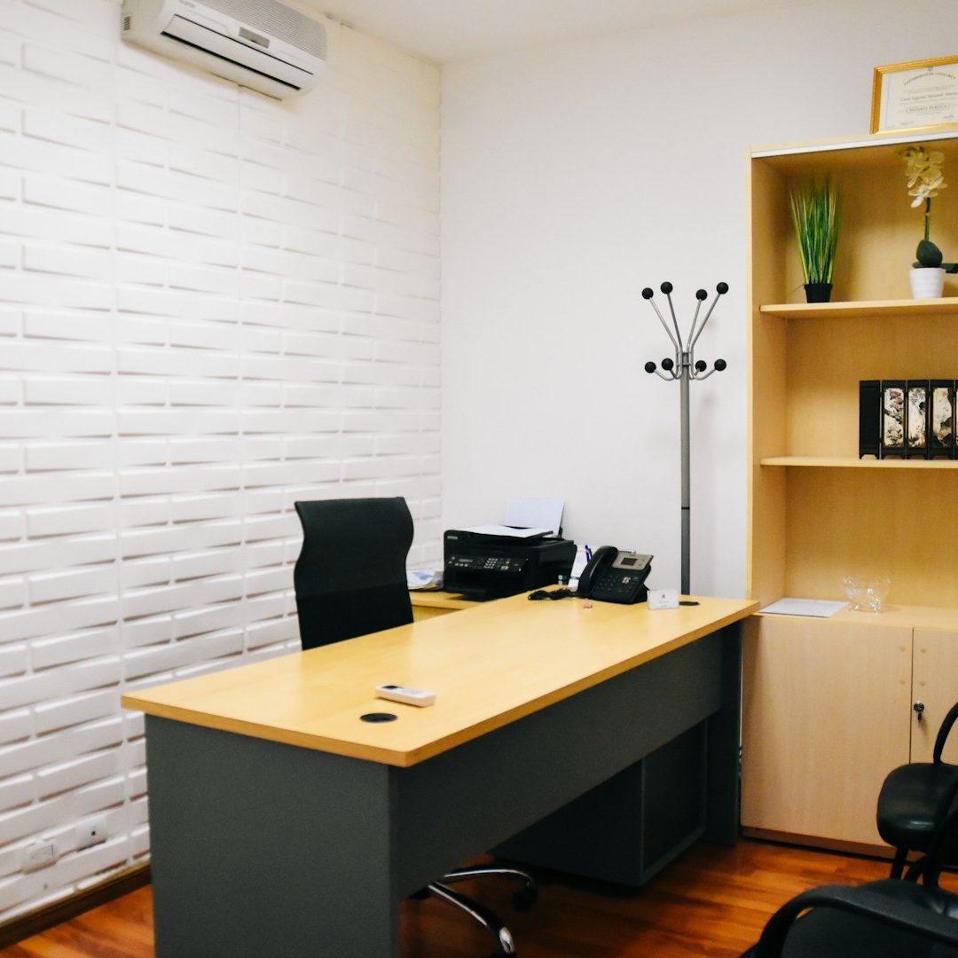 An office space with a desk, chair, bookshelf, and wall-mounted air conditioning unit.