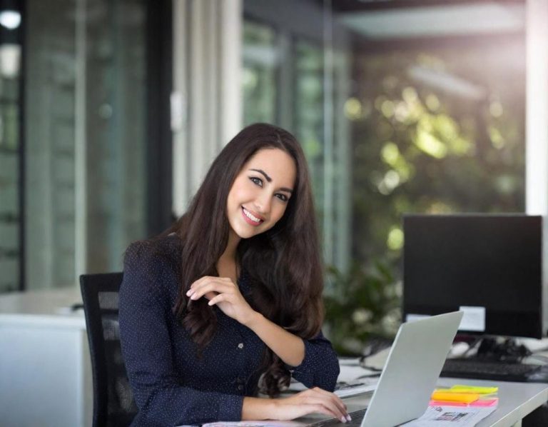 IT consultation A smiling woman working on a laptop in a bright office setting.